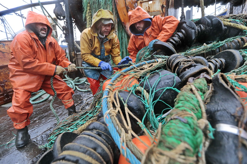 Under driving rain, fishermen aboard the New Bedford fishing boat Sao Paulo, (l to r) Tony Borges (owner/captain), Joao Gomes, and Joshua Azul  change the nets from groundfish, to fluke netting in preparation for January 1st when the new fluke regulations will be put into effect. PHOTO PETER PEREIRA