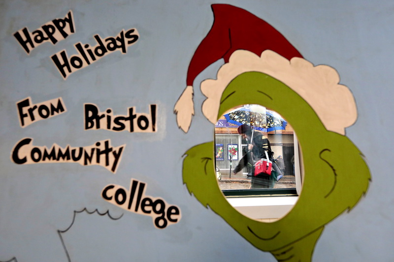 A woman walking up William Street in downtown New Bedford, MA fights the driving rain with umbrella in hand, as seen through the Grinch cutout installed in the Community Room of the lower lever at the Bristol Community College downtown Campus for a future holiday event, where students will be able to put their face inside to take photos as the Grinch.   PHOTO PETER PEREIRA