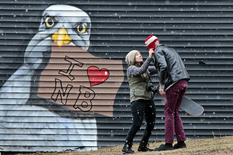 Photographer Kat Knutsen adjusts the hat that Logal Raposo is modeling, in front of a mural painted on a wall at Wings Court in downtown New Bedford, MA as snow starts to fall across the region. PHOTO PETER PEREIRA