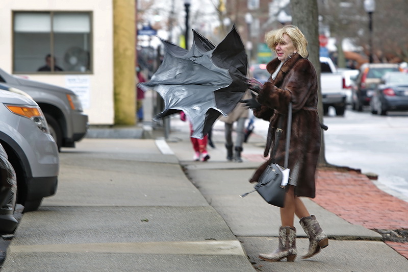 A woman walking up Elm Street in downtown New Bedford, MA struggles to control her umbrella, as high winds and rain sweep over the region.  PHOTO PETER PEREIRA