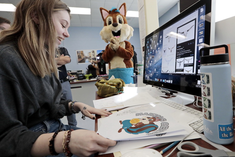 Chippy looks on as Sara Gifford, 18, pulls out the drawings she and her classmates made during the design process, when they came up with the New Bedford Credit Union's mascot. Chippy the New Bedford Credit Union's mascot, made a surprised visit to Visual Design class at Voc-Tech in New Bedford.  Students of Visual Design were responsible for the creation of the design of the mascot for the credit union's Making Cents Kids Account program and were unaware that an actual physical mascot was going to be made.  PHOTO PETER PEREIRA