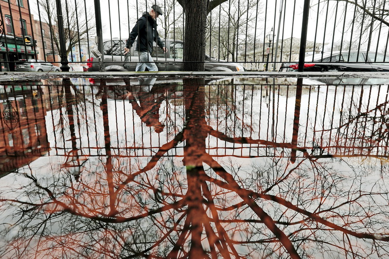 A man and a tree are reflected on a flooded arear, as he walks up Acushnet Avenue past Custom House Square in downtown New Bedford., MA.  PHOTO PETER PEREIRA