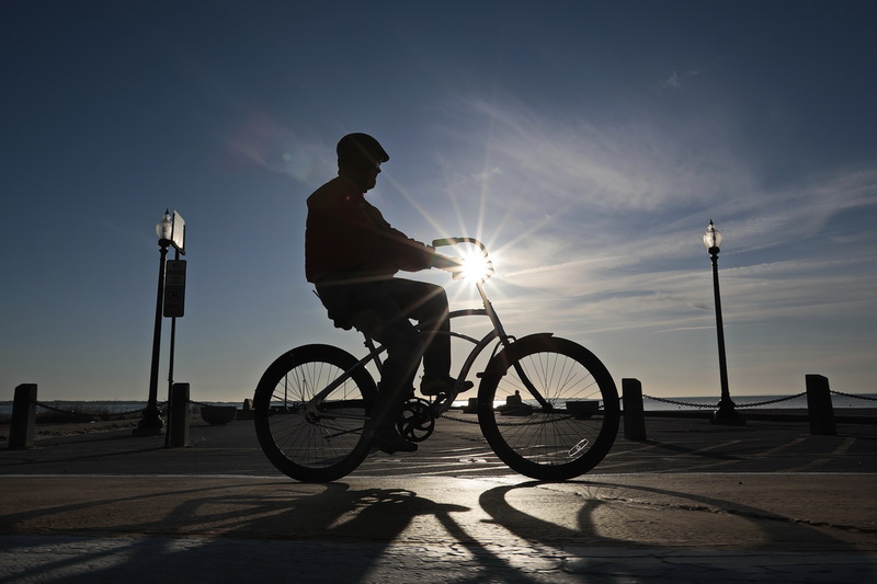 A man takes a ride on his bicycle around the south end of New Bedford, MA as the sun rises in the distance.   PHOTO PETER PEREIRA