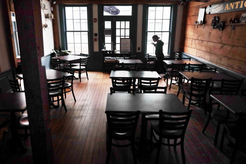 Jessica Coelho Arruda, speaks on the phone, as she walks past an empty dining room which is usually filled during the breakfast hours.  Tia Maria's European Caf in downtown New Bedford had switched to take-out due to the recent coronavirus pandemic, and is now exploring the possibility of delivery service as well.  PHOTO PETER PEREIRA