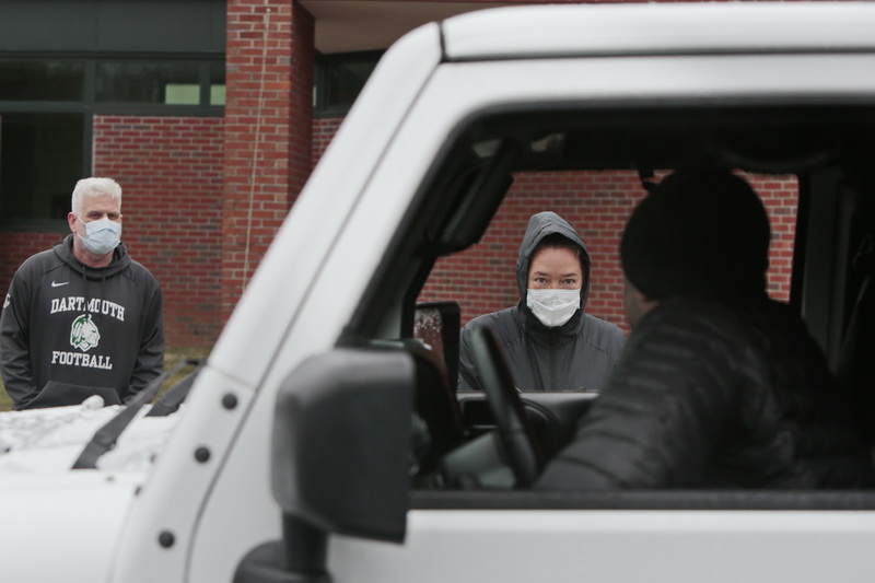 Dartmouth Middle School assistant principal, Peter Rossi, and Helen Mitchell, Instructional Technology Specialist, speak with a parent inside their vehicle, before placing a laptop on a table next to the car for the parent to pick up in a zero contact exchange.  PHOTO PETER PEREIRA