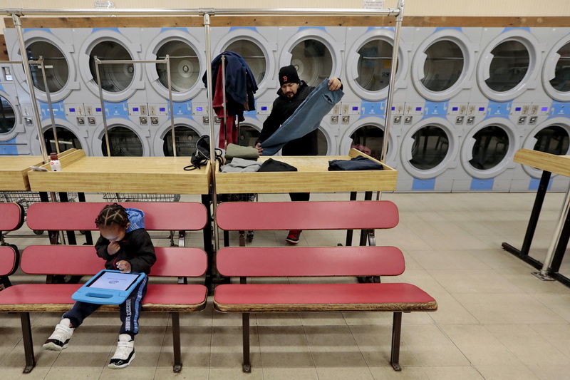 A young boy plays on his tablet, as his father does laundry, while in the background A.J. Adrian folds his clothes after washing them at the Lincoln Laundromat on Acushnet Avenue in New Bedford.  Customers are asked to leave the laundromat as their clothes wash.  PHOTO PETER PEREIRA