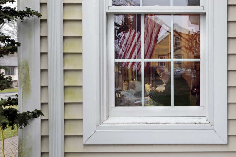 An American flag hanging outside is reflected on the window, as Deolinda Roda can be seen volunteering her skills to make over 70 masks for St. Lukes and Charlton Hospital nurses at her daughters house in Dartmouth, MA.   PHOTO PETER PEREIRA