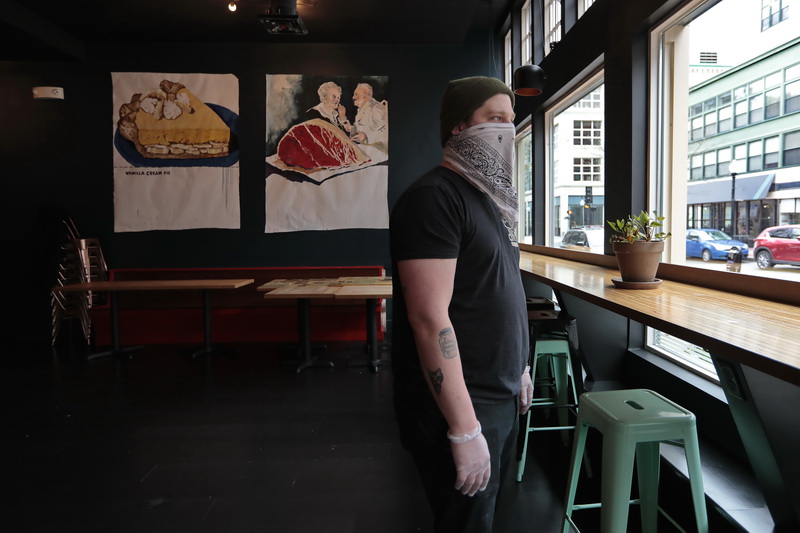 With a protective hankerchief over his mouth, Josh Lemaire owner of dNB Burgers, looks out the front windows of his restaurant in downtown New Bedford, behind him, the dining room usually filled with tables lies empty. The downtown eatery has re-opened for take-out with it's opening hours restricted from 4-8pm.  PHOTO PETER PEREIRA