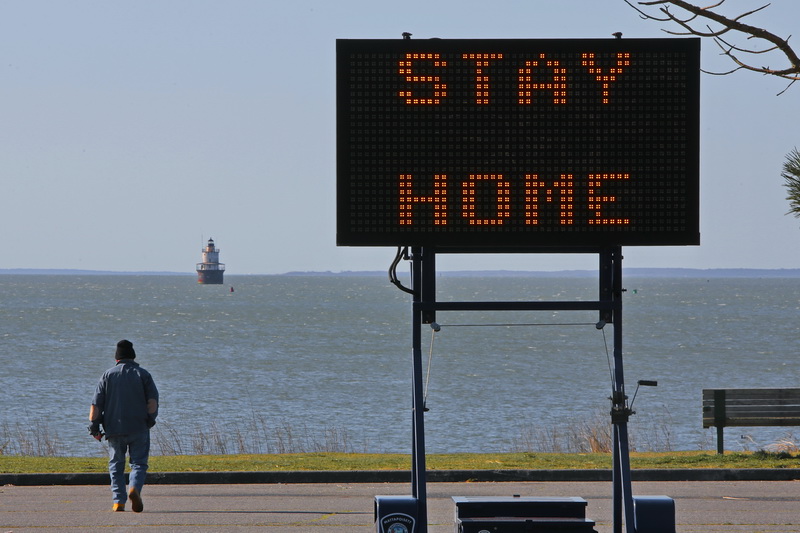 A sign urges residents to stay home as a man makes his way across the Fort Phoenix parking lot in Fairhaven, MA. PHOTO PETER PEREIRA