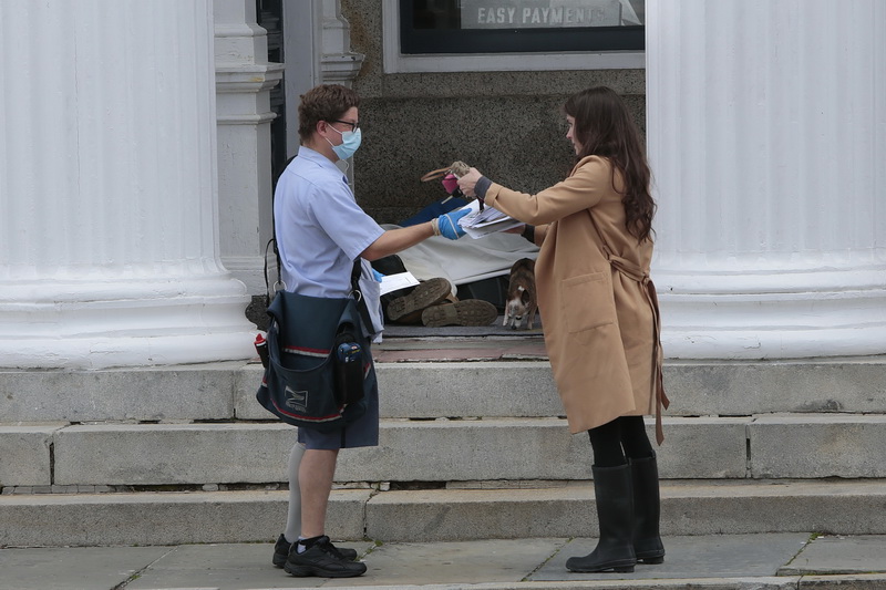 A postal worker hands a woman her mail as a homeless man's boots can be seen in the background sleeping at the entrance to a building in downtown New Bedford, MA. 