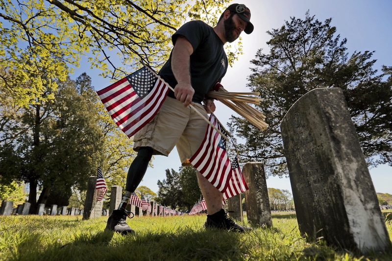 Christopher Gomes, veteran agent for the city of New Bedford, places American flags at the graves of veterans buried at the Pine Grove Cemetery, in preparation for Memorial Day.  Mr. Gomes, an Army veteran, lost his right leg when an IED exploded while serving in Iraq in 2008. PHOTO PETER PEREIRA