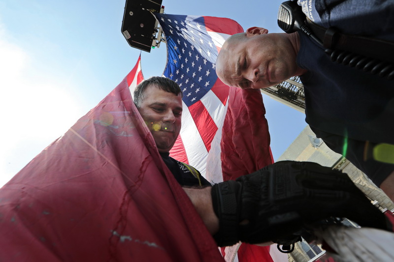 New Bedford firefighters Miguel Cabral and Capt. Kurt Houghton hoist a giant American flag in preparation to celebrate Fr Mike Racine's 25th anniversary of his ordination, held in the parking lot of the Saint Lawrence church in New Bedford, MA.  PHOTO PETER PEREIRA