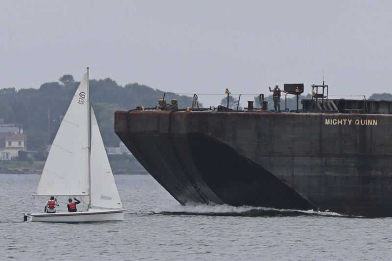 Sea Lab instructors wave at a worker on the deck of the massive Mighty Quinn barge heading into New Bedford harbor.  The Sea Lab is filming footage on how to sail for a virtual sailing class which they are filming off of East Beach in New Bedford. The virtual program is being sponsored by the Naval Undersea Warfare Center.    PHOTO PETER PEREIRA