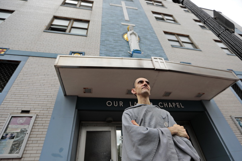 A statue of Mary looks down from above as Franciscan friar Pedro Olheiro stands in front of Our Lady's Chapel on Pleasant Street in New Bedford, waiting to be picked up by Father Matthias Sasko, after which the two will visit a man fighting cancer at this home in New Bedford, MA.  PHOTO PETER PEREIRA