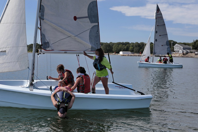 A student takes refuge from the extreme heat by dipping his head into the water, as his fellow sailing students head out for a sail as the Community Boating Center starts the Summer Your Sailing Program with new protocols in place to keep the students safe in Clarkes Cove in New Bedford, MA