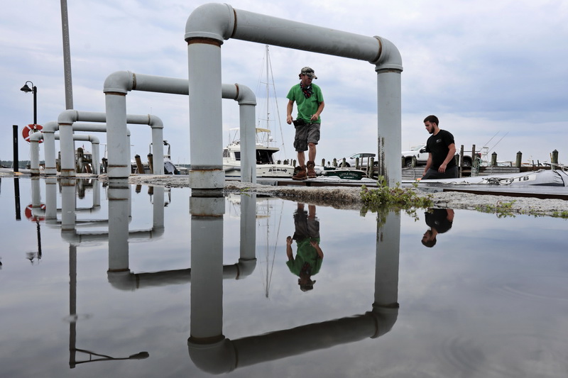 Jason Costa and Danny Oliveira of Triad Boatworks are frames by the dock supports and reflected by the puddles of rain water, as they place a sea skiff in the water to establish the waterline at the wharf in Mattapoisett, MA.  PHOTO PETER PEREIRA