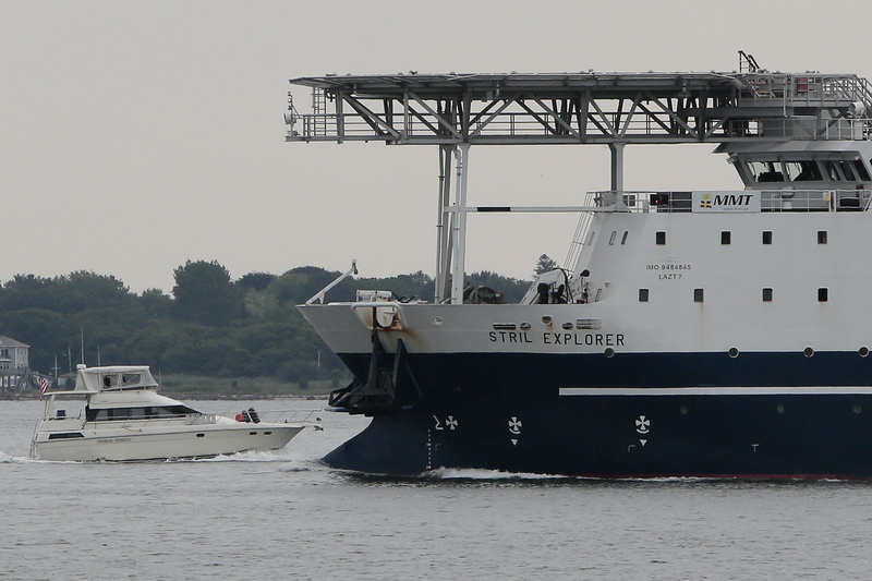 A small pleasure craft makes its way past the Stril Explorer, a mammoth subsea operations support vessel featuring a helicopter landing pad on top, heading back into New Bedford harbor. PHOTO PETER PEREIRA