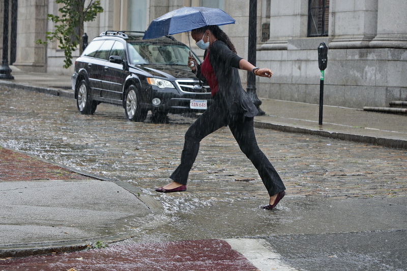 A woman tries to jump over the stream of water making its way down William Street in downtown New Bedford, MA as heavy rains sweep across the region.  PHOTO PETER PEREIRA