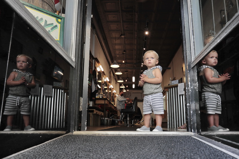 Oliver Antil, 18 months, takes a look outside from the entrance of New Bedford Barber Co., as his brother Landon Crowley, 8, gets a haircut from Jeff St.Claire in the background. PHOTO PETER PEREIRA