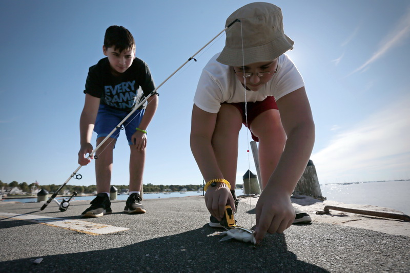 Jayden Dalomba, 12, uses a measuring tape to record the size of the scup fish that his cousin Devin Dalomba, 12, caught (7.5 inches) in Mattapoisett, MA.  Because it was undersized, they threw it back in.  PHOTO PETER PEREIRA