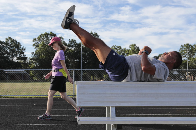 A woman walks past, as Jamie Luisi works out on top of a seat at Cushman Park in Fairhaven, MA.  PHOTO PETER PEREIRA