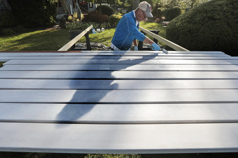 John Blanchette's shadow dances across the mahogany planks he is priming for a screened porch being constructed at a home in Fairhaven, MA. PHOTO PETER PEREIRA