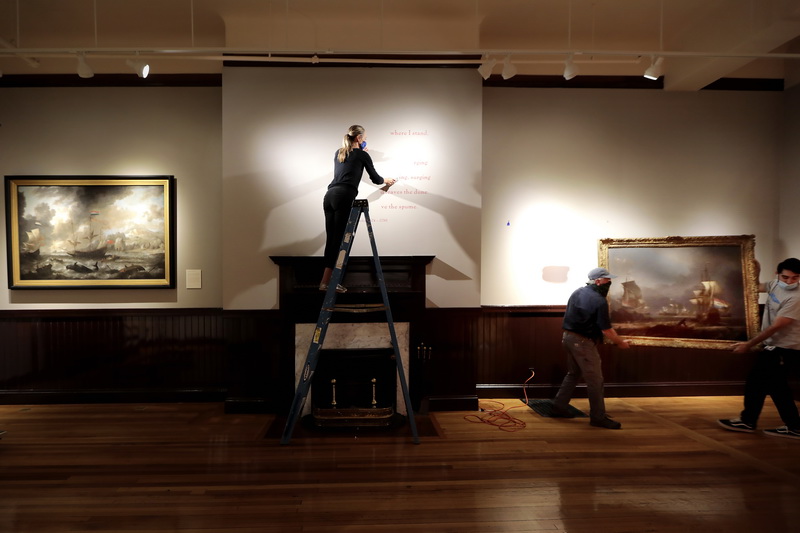 Christina Connett Brophy, chief curator of the Whaling Museum, removes the lettering on the wall from the previous show, which featured Dutch paintings on exhibit in the Wattles Gallery Room, in preparation for the next exhibit entitled A City for the Arts: Masterworks of Greater New Bedford. Below Michael Dyer and Eric Franco remove one of the pieces from the De Wind is Op: Climate, Culture and Innovation in Dutch Maritime Painting, to make way for the new show which is scheduled to open later this month. 