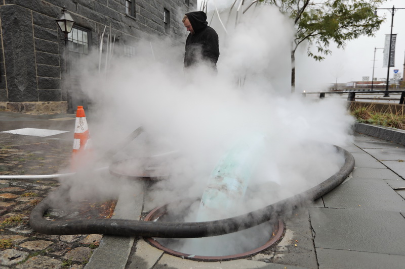 Steam billows upward from the manhole in the foreground, as John Davis of Green Mountain Pipeline is monitors the meters while hot steam shrinks the liners to the freshly cleaned sewer line in front of the Buzzards Bay Coalition building in downtown New Bedford, MA. PHOTO PETER PEREIRA