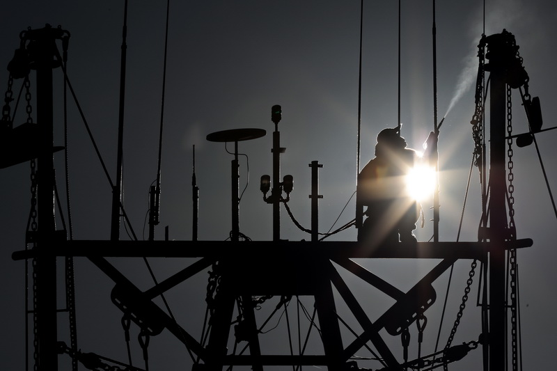 The sun rises in the distance as a painter finds himself high above New Bedford harbor using a portable high pressure air gun to remove the existing paint from the masts of a fishing boat, before giving it a fresh coat of paint.    PHOTO PETER PEREIRA