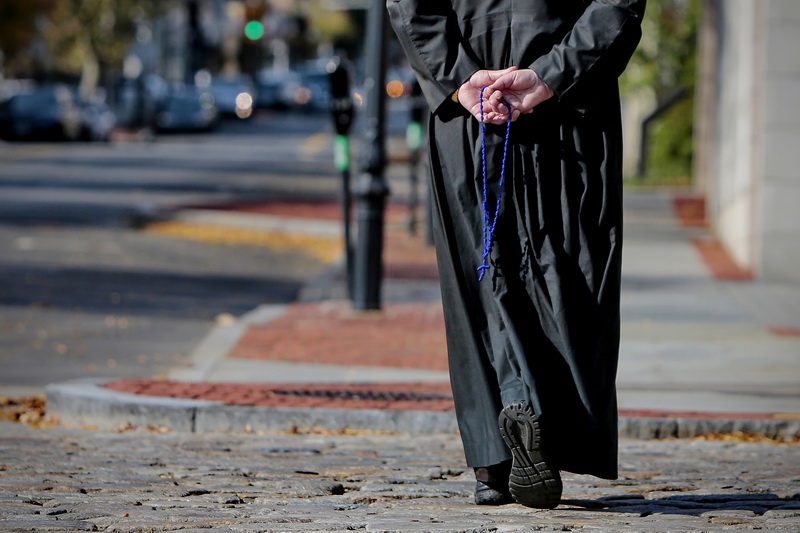 A man wearing long robes hold a rosary behind his back as he makes his way up Union Street in downtown New Bedford, MA. PHOTO PETER PEREIRA