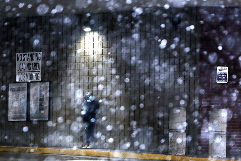 A woman takes shelter from the first snowfall of the season under a light inside the bus terminal in downtown New Bedford, MA. PHOTO PETER PEREIRA