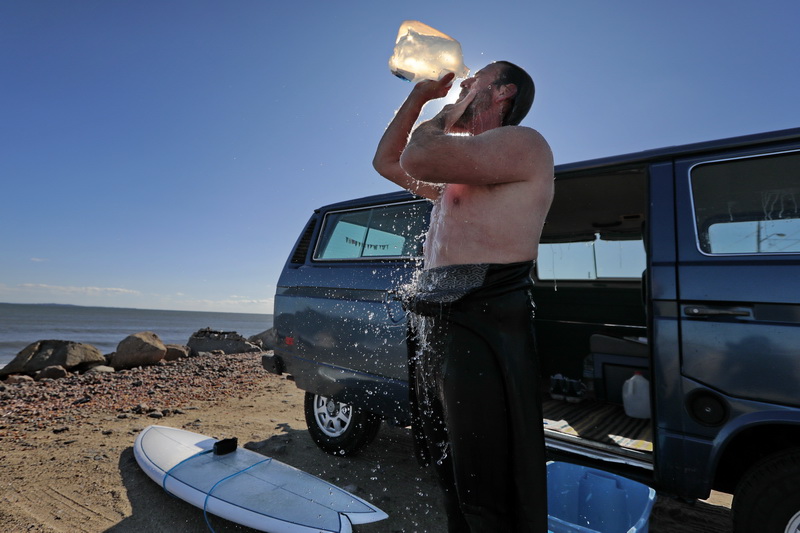 Dan Goulart washes the salt water from his face using a bottle of fresh water, after surfing the higher than normal waves at Horseneck Beach in Westport, MA.  PHOTO PETER PEREIRA