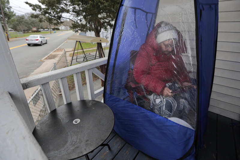 Lillian Goneville watches a program on her tablet inside one of the two small tents she set up on the porch outside her home in Fairhaven, MA to spend some time outside while staying warm and still being isolated.   PHOTO PETER PEREIRA