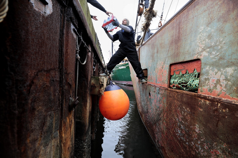 With one leg on the dock and another on the boat, Aidan Rodrigues and fellow crewmembers of the scalloper Ocean Leader, load food supplies before heading out to sea from New Bedford harbor.    PHOTO PETER PEREIRA