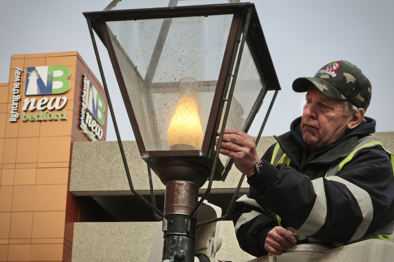 Joe Brune an electrician with the city of New Bedford, changes the light bulb on one of the streets iconic light poles.  In the background the sign atop the public parking garage states 'New Bedford lighting the way' a reminder of a time the city was called the 'city that lit the world'.  PHOTO PETER PEREIRA 