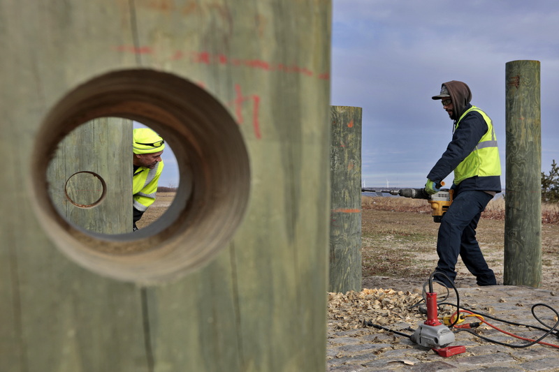 Helder Baptista, left (seen through one of the holes that he and fellow members of New Bedford DPI made) keeps his eye on the horizontal alignment for the hole that Danny Pacheco is making using a drill with an auger on one of the posts that will become part of a future fishermen memorial.  The memorial will feature an anchor with a heavy chain running through the holes they are making.  PHOTO PETER PEREIRA 