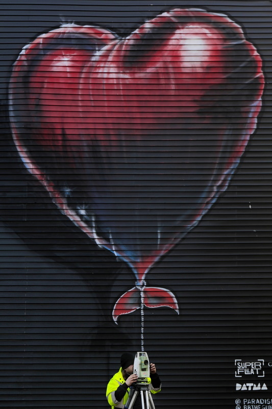 John Young is seemingly going for a ride on a heart shaped balloon painted on the side of a building, as he takes survey measurements of a property adjacent to Wings Court in downtown New Bedford. PHOTO PETER PEREIRA