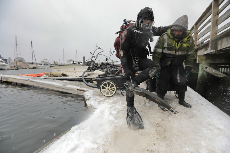 John Hughes holds onto Marco Lopez for support, as he puts on his fins before diving into the frigid waters around Pope's Island Marina in New Bedford to install inflatable bags around the boat which caught fire this weekend.  The boat will be towed to the Tucker-Roy Marine & Salvage yard where the cause of the fire will be investigated. PHOTO PETER PEREIRA