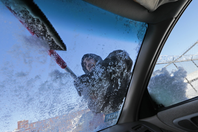 Jose Brown uses a brush in an effort to remove the ice built up on his windshield on his car parked in New Bedford, from the snowfall which swept over the region this weekend.  PHOTO PETER PEREIRA