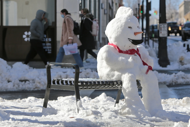 A snowman wearing a mask, sits on the bench at the intersection of Purchase Street and Union Street in downtown New Bedford, MA as pedestrians make their way on the sidewalk in the background  PHOTO PETER PEREIRA