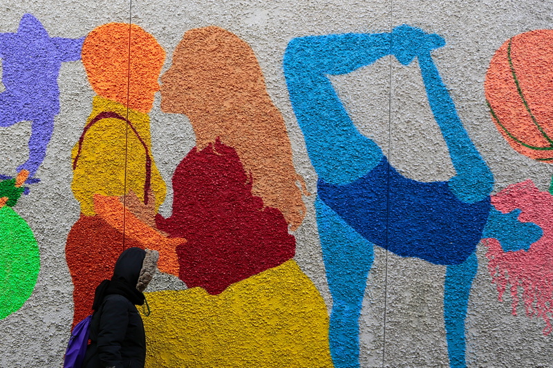 A woman walks past a colorful mural painted on the wall of the Police Station on Sears Court in downtown New Bedford, MA. PHOTO PETER PEREIRA