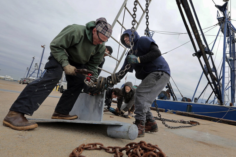 Captain George Bradgon, left, Alex Cruz, right, and the crew of the Resilient install a new chain for the winter outrigger, on the fishing boat docked at State Pier in New Bedford, MA.  PHOTO PETER PEREIRA