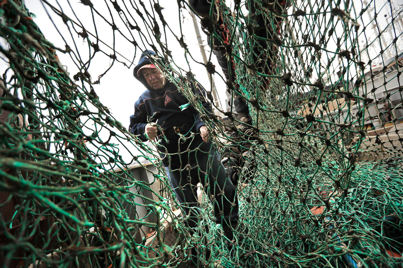 Jose Braz cuts away the section of the net that has rotted away, as he makes repairs to the nets aboard the fishing boat Hera, docked in New Bedford, MA. PHOTO PETER PEREIRA