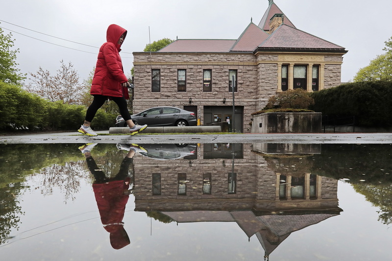 A woman is reflected in a large puddle, as she passes the iconic Milicent Library in Fairhaven on a rainy morning walk. PHOTO PETER PEREIRA