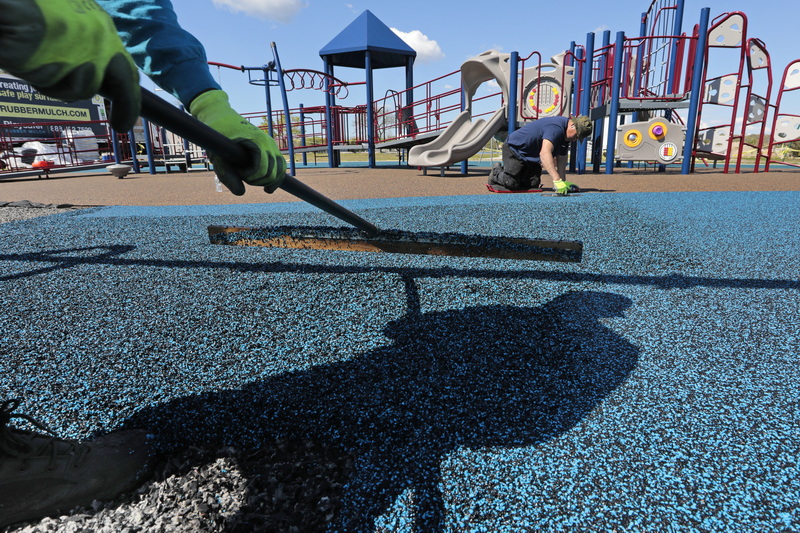 Javier Munoz is joined by the shadow of Antonio Barradas as they install the colorful, rubbery, soft surface at the new playground they are constructing on Apponagansett Beach in Padanaram. PHOTO PETER PEREIRA