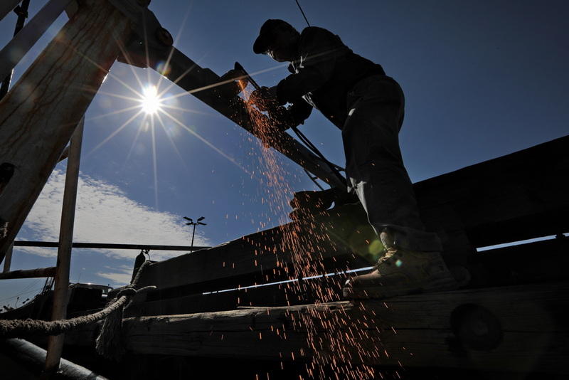 Joao Lopes of Luzo Welding Services sends spakrs flying as he uses a cutting torch to put a hole in a new outrigger he is installing on the Seven Seas fishing boat in New Bedford.  PHOTO PETER PEREIRA