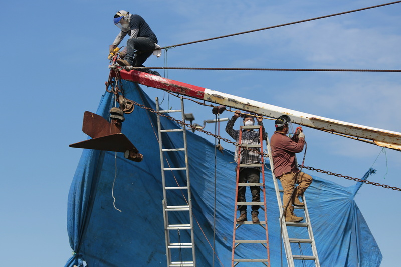 Painters remove the rust from the outrigger of the fishing boat Fisherman, before applying a fresh coat of paint in New Bedford, MA.  PHOTO PETER PEREIRA