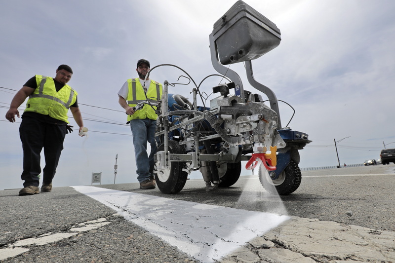 Kurt Charbonneau uses a line painter to re-paint the crosswalk lines across West Rodney French Boulevard in New Bedford, MA as Mark Verdejo drops reflective crystals onto the fresh paint.  PHOTO PETER PEREIRA