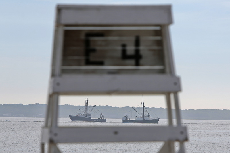 A fishing boat heads out to sea, as another comes into New Bedford harbor, as seen through the gap of a lifeguard chair at East Beach in New Bedford, MA. PHOTO PETER PEREIRA