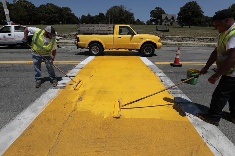 A yellow pickup truck drives past, as Kurt Charbonneau and Mark Verdejo re-paint the yellow crosswalk on the south heading side of West Rodney French Boulevard in New Bedford, MA. PHOTO PETER PEREIRA